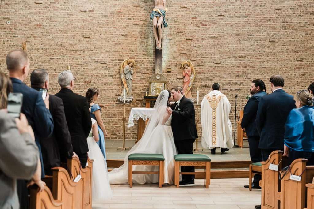 Bride and groom sharing their first kiss as husband and wife at the altar inside Our Lady of Good Counsel Church