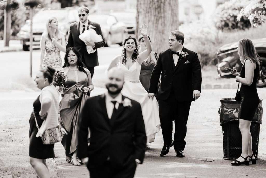 Bride and groom walking with bridal party toward Booth Park in Nutley, captured in a candid joyful moment