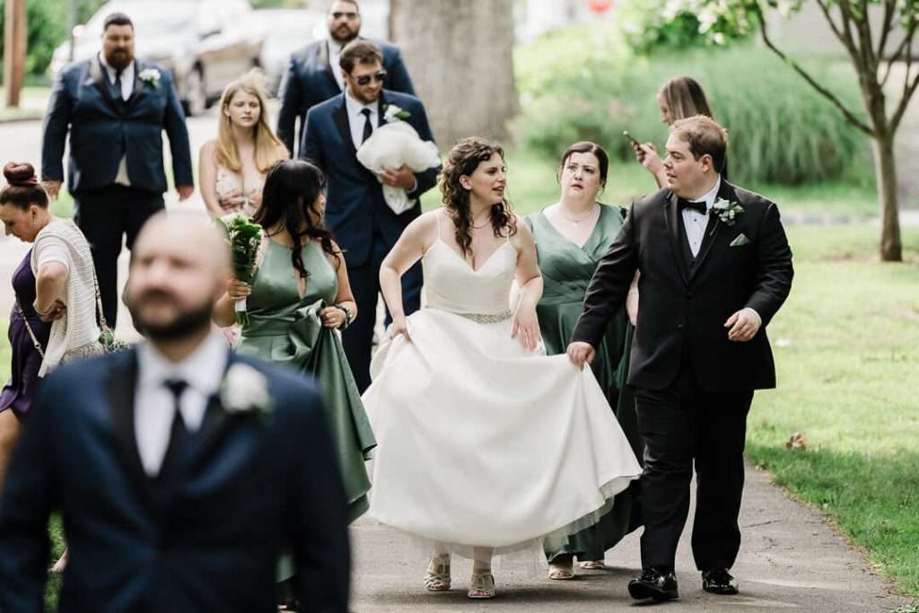 Bride and groom holding hands and smiling as they walk through Booth Park in Nutley, NJ