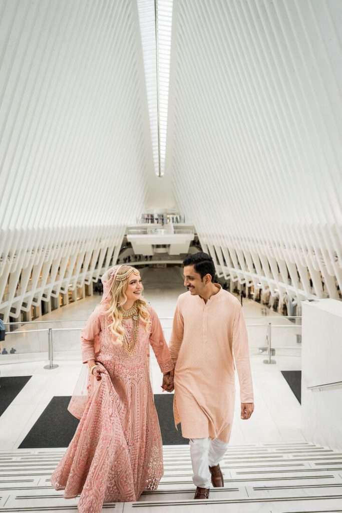 Smiling couple walking up the steps inside the Oculus during a vibrant NYC engagement session, photographed by Alex Kaplan, New York wedding and engagement photographer.
