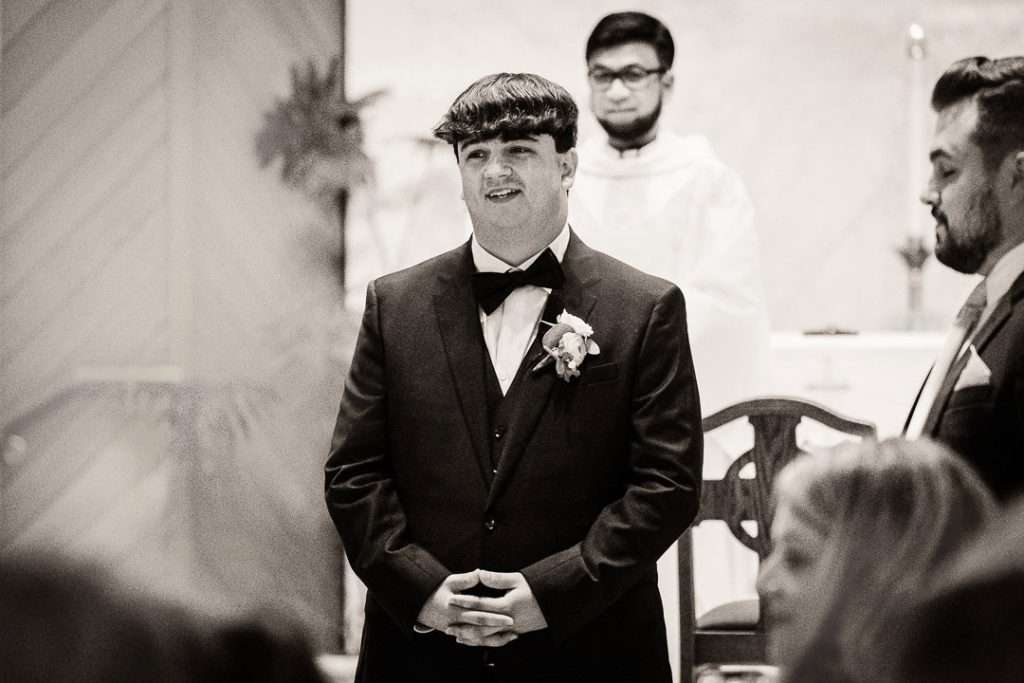 Groom stands at the altar, smiling warmly as he sees his bride entering the church at Notre Dame of Mt. Carmel Roman Catholic Church.