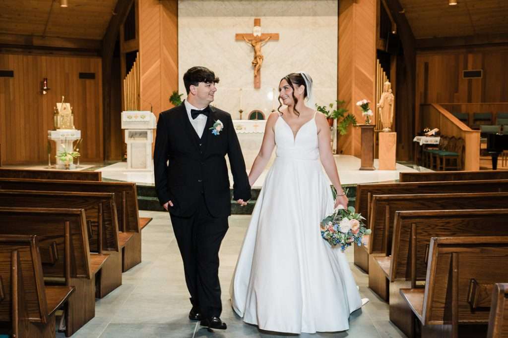 Bride and groom walk hand-in-hand up the aisle with joyful smiles, bouquet in hand, after being pronounced married.