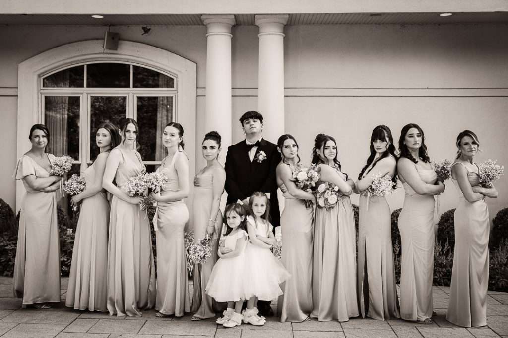 Bride and groom pose with bridesmaids, groomsmen, and flower girls outdoors at The Mansion at Mountain Lakes in coordinated blush and navy tones.