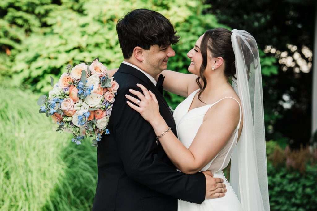Bride and groom share a laugh while walking through the gardens, captured in a candid moment at The Mansion at Mountain Lakes.