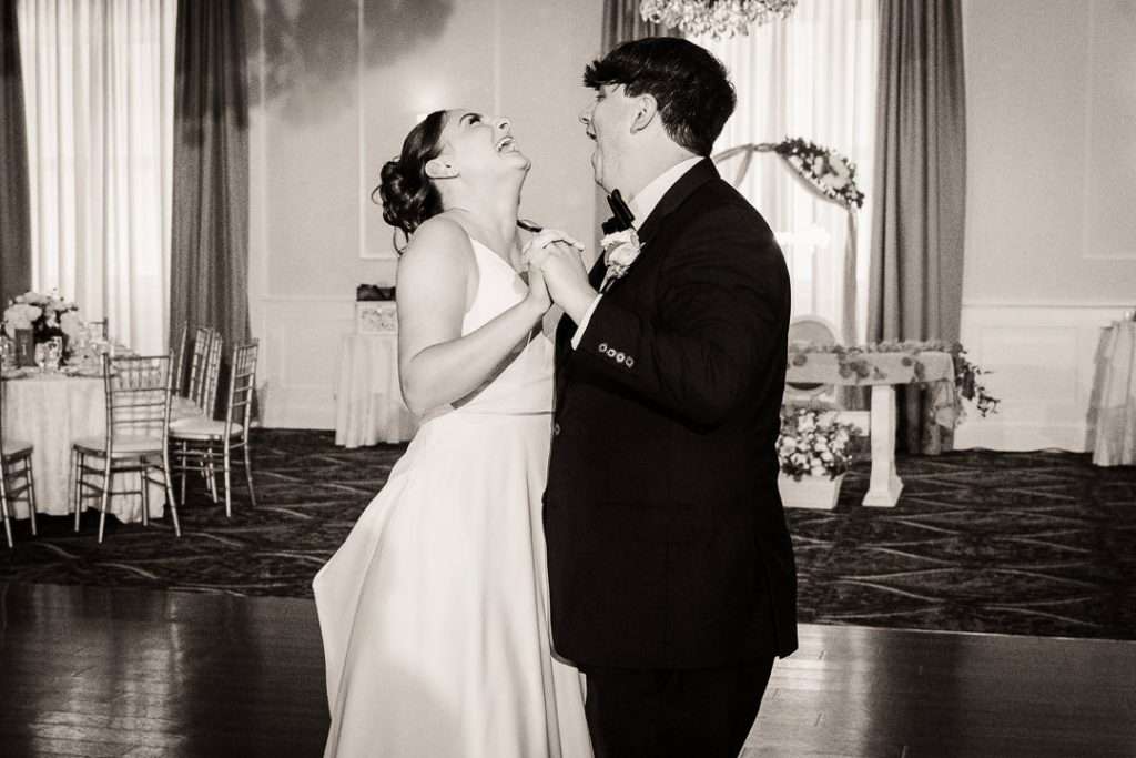 Bride and groom laugh mid-spin during their first dance on the reception floor, surrounded by soft uplighting and elegant decor.