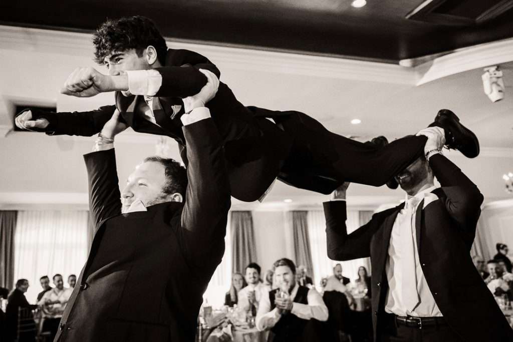 Groomsmen lift one of their own in a Superman flying pose, creating a hilarious and energetic group shot during the wedding intros.