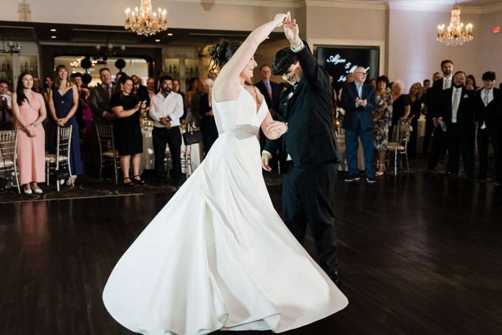 Bride twirls gracefully while holding the groom’s hand on the dance floor, captured in motion during their reception celebration.