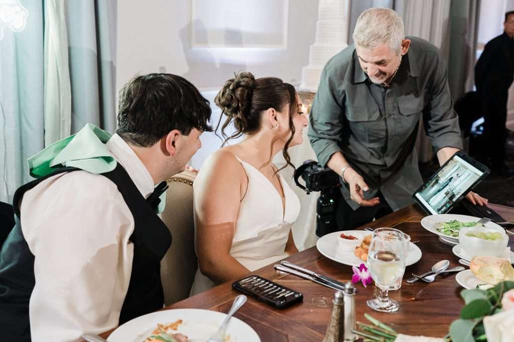 Bride and groom looking at wedding photos on an iPad during their reception at The Mansion at Mountain Lakes, NJ, while the photographer shows them a sneak peek.