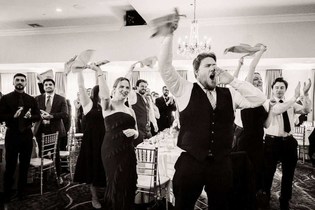 Wedding guests waving napkins and cheering enthusiastically during the reception at The Mansion at Mountain Lakes in New Jersey.