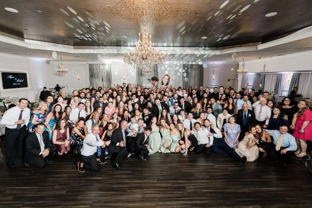 Large group wedding photo with all guests smiling and gathered on the dance floor at The Mansion at Mountain Lakes in New Jersey.