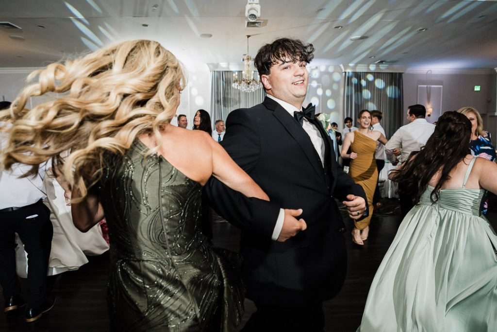  Groom dancing with guests, smiling and spinning during the wedding celebration at The Mansion at Mountain Lakes.