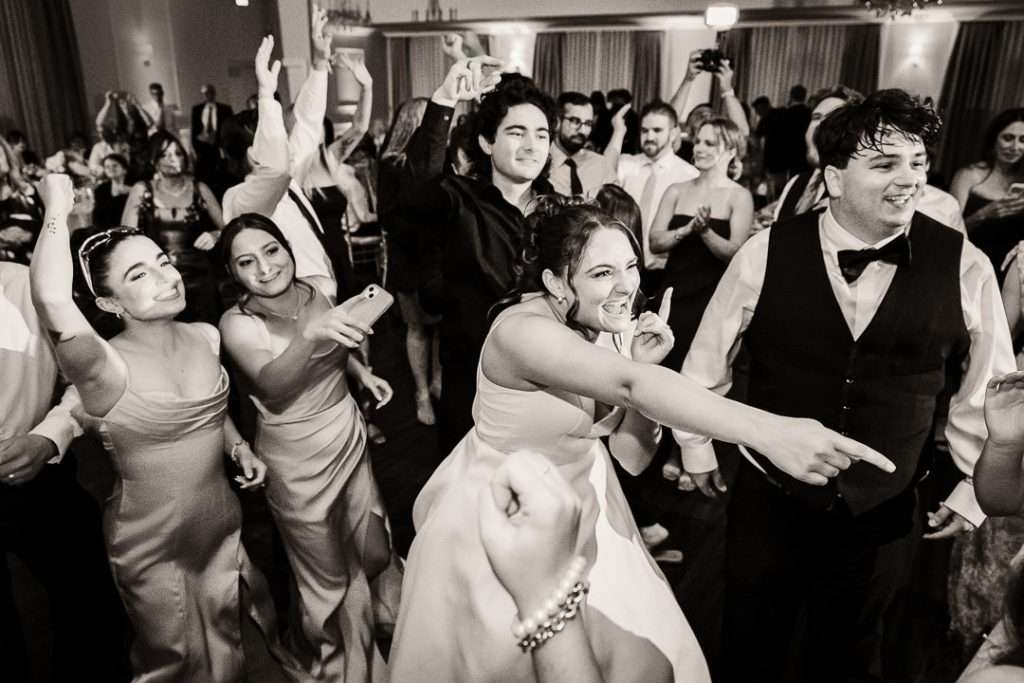 Bride smiling and pointing while dancing with guests during a high-energy wedding reception at The Mansion at Mountain Lakes.