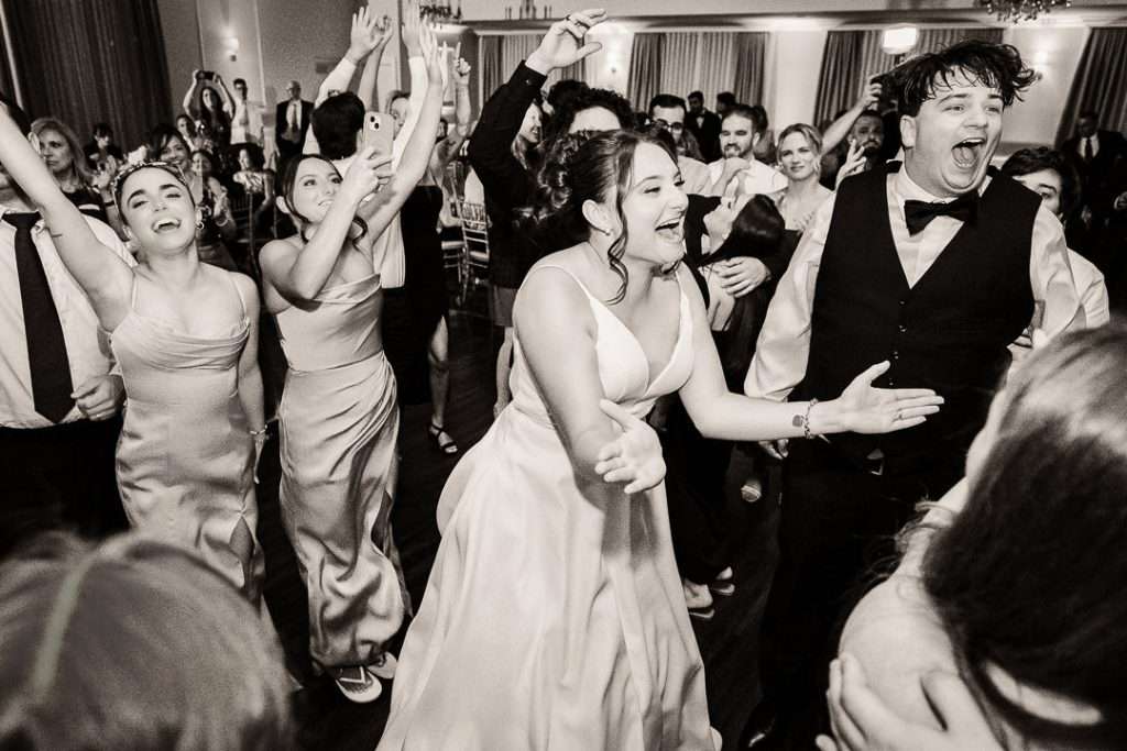 Wedding guests and newlyweds celebrating on the dance floor with hands raised and joyful expressions at The Mansion at Mountain Lakes