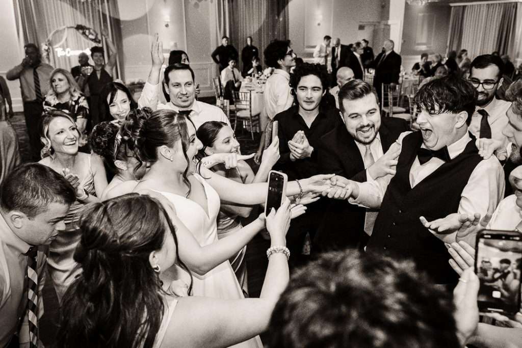 Bride and groom laughing and holding hands, surrounded by friends and family during a dance circle at their wedding reception at The Mansion at Mountain Lakes.