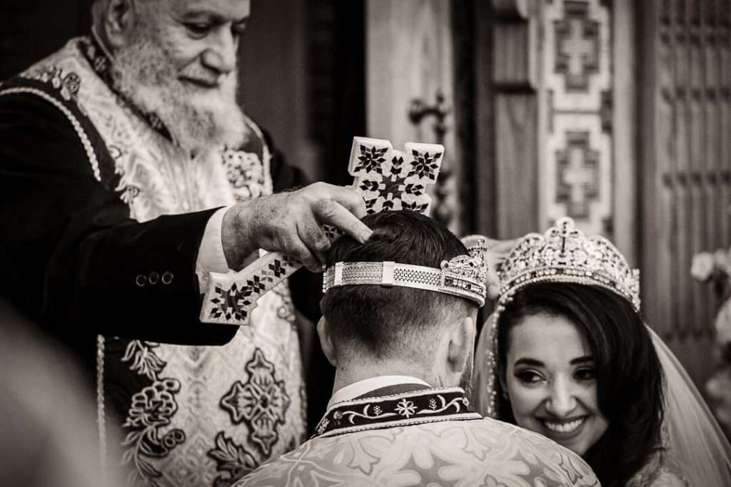 Coptic wedding crowning ceremony with priest blessing groom and bride smiling