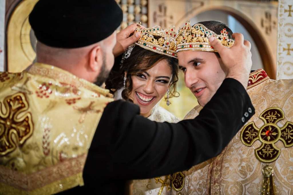 Priest crowns smiling bride and groom during Coptic Orthodox wedding ceremony.
