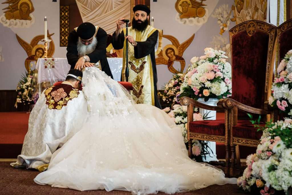 Coptic priest lays his hands on the couple in a solemn moment of final blessing while they bow their heads at the altar.