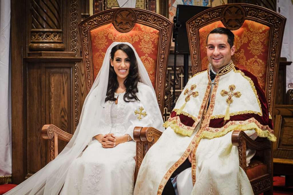 Bride and groom sit on ceremonial thrones wearing traditional Coptic Orthodox wedding robes.