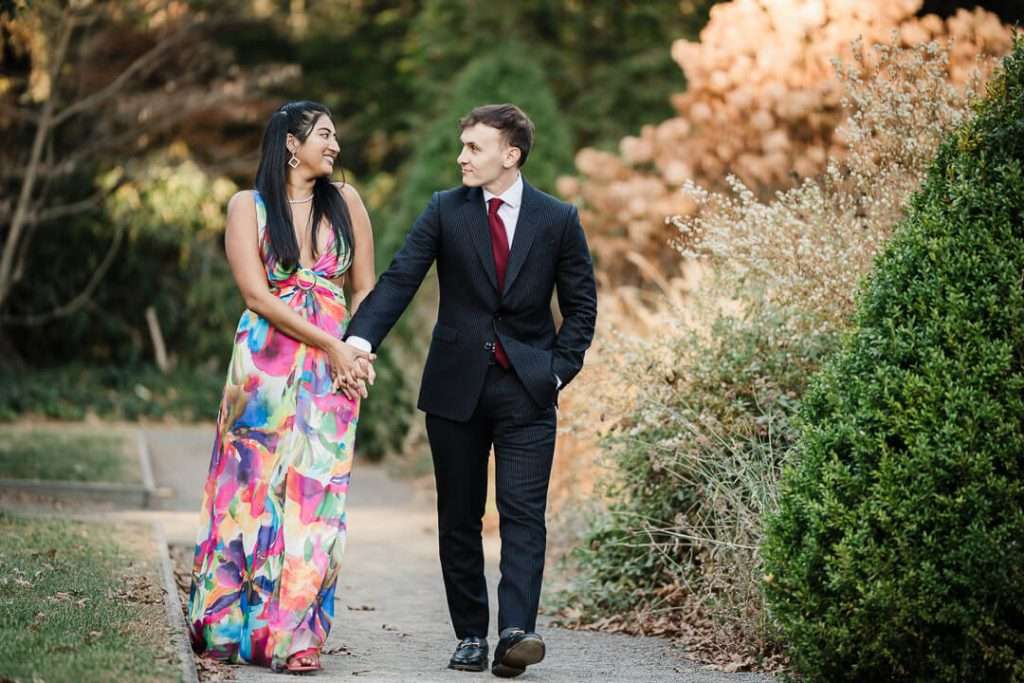 Engaged couple walking hand-in-hand through the garden paths at Van Vleck House, smiling at each other in the golden afternoon light.
