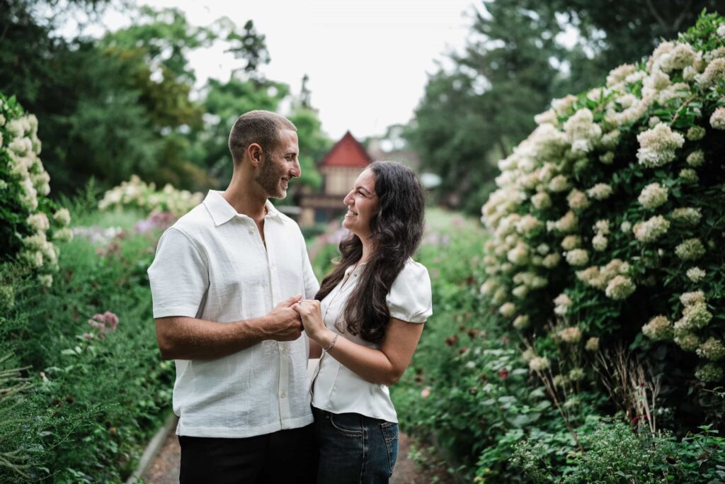 Engaged couple holding hands between hydrangea borders at Van Vleck House and Gardens in Montclair NJ
