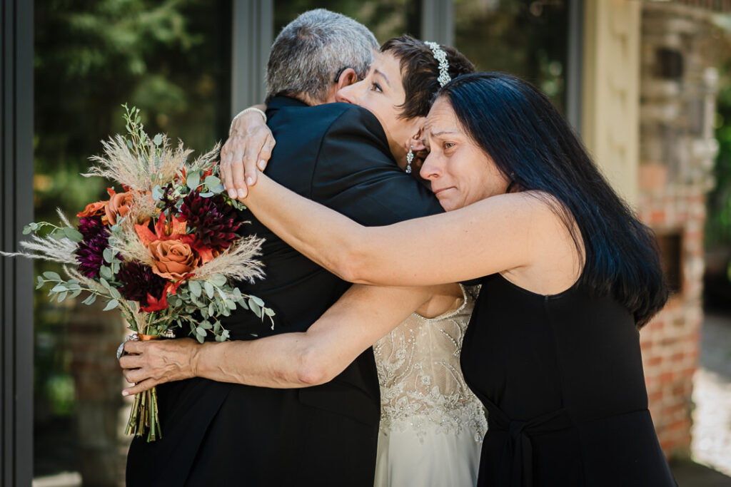 Bride embracing family members during portraits at Mohawk House, holding a fall bouquet with copper and burgundy tones.