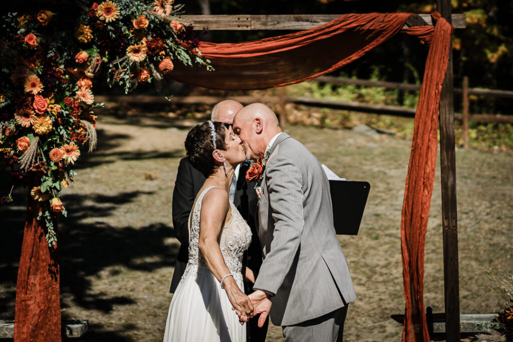 First kiss at Mohawk House wedding ceremony - couple under fall floral arbor Sparta NJ