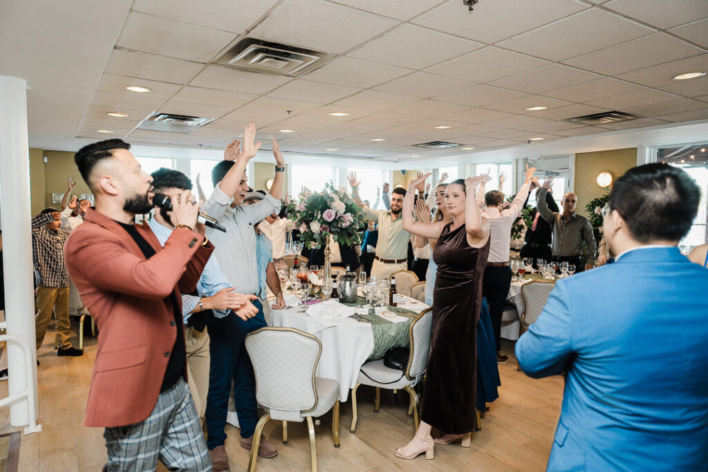 Guests raising their hands and cheering as a singer entertains the crowd during a lively engagement celebration at The Armory NJ Restaurant in Perth Amboy, photographed by Alex Kaplan Photography.