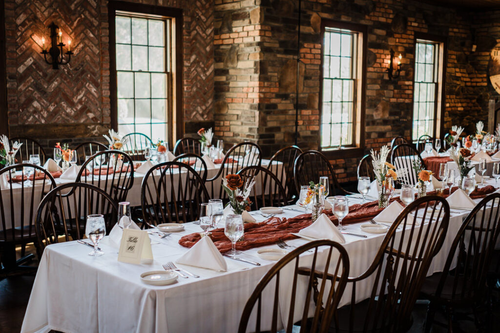 Rustic reception tables set with white linens, copper runners, and fall florals inside Mohawk House.