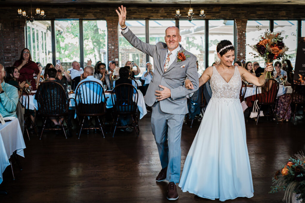 Bride and groom making their grand entrance into Mohawk House reception, waving and smiling as guests cheer.