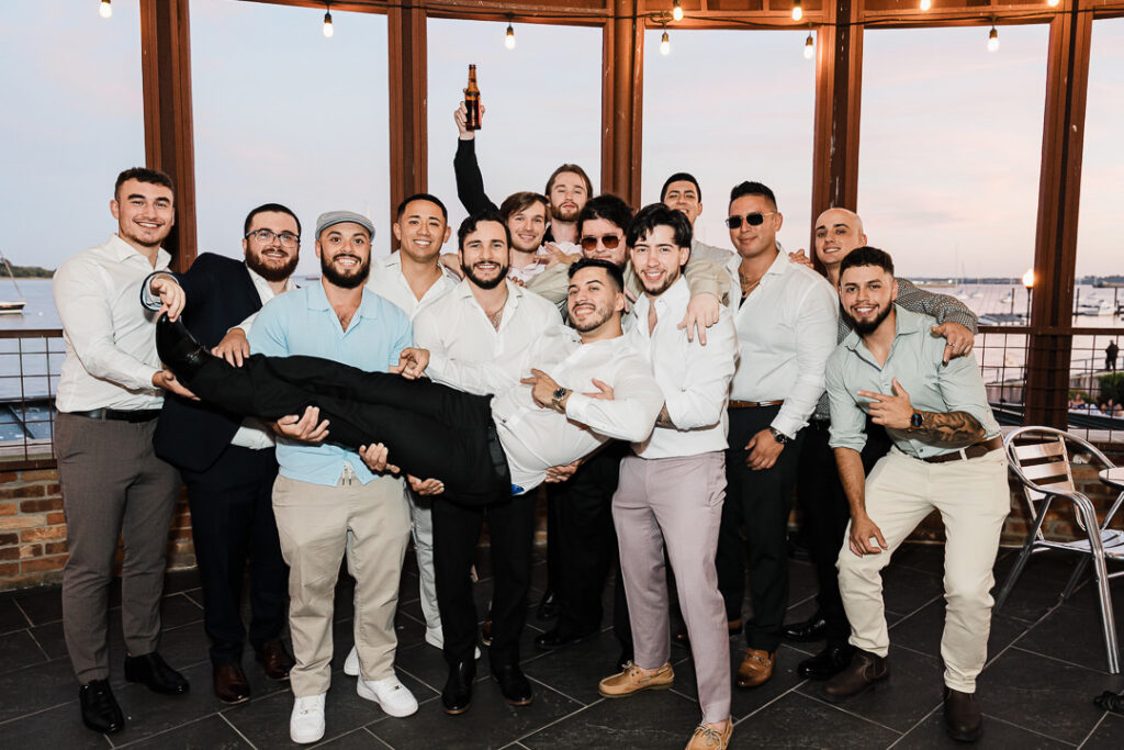 Groom lifted by friends during sunset celebration on the waterfront terrace at The Armory NJ Restaurant in Perth Amboy, photographed by Alex Kaplan Photography.