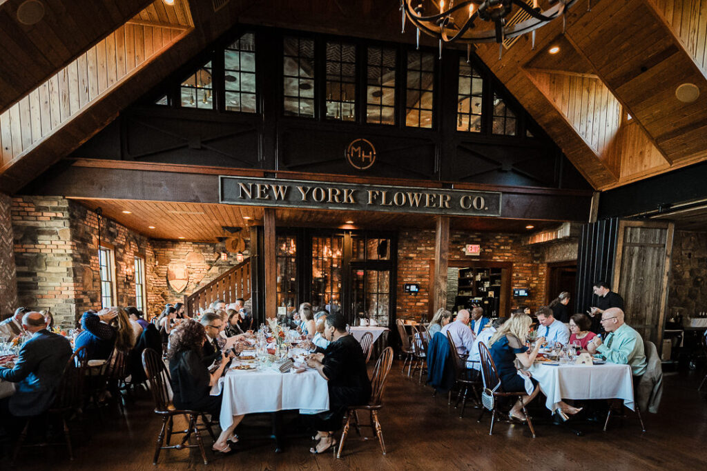 Wide view of Mohawk House reception with guests dining under rustic wooden beams and warm lighting.