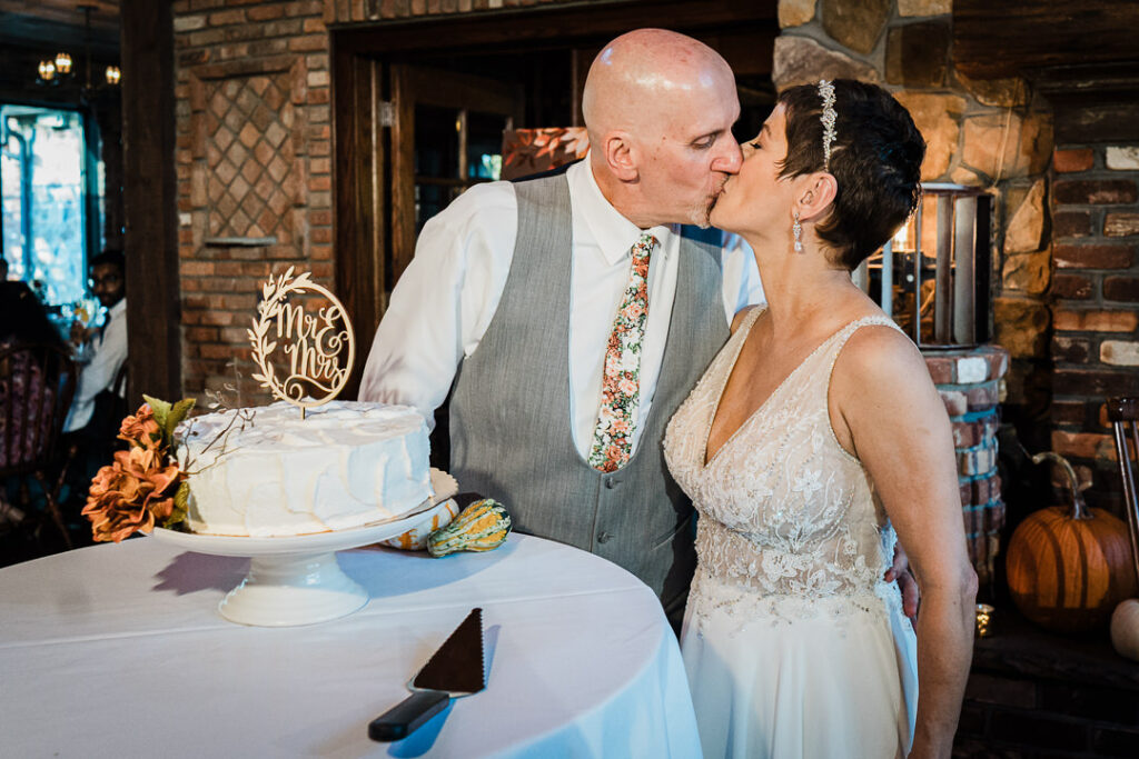 Bride and groom kissing beside their fall-themed wedding cake at Mohawk House.