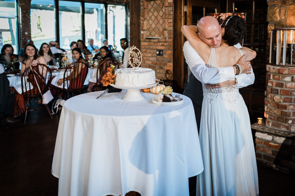 Couple embracing during cake cutting at Mohawk House, surrounded by cheering guests.