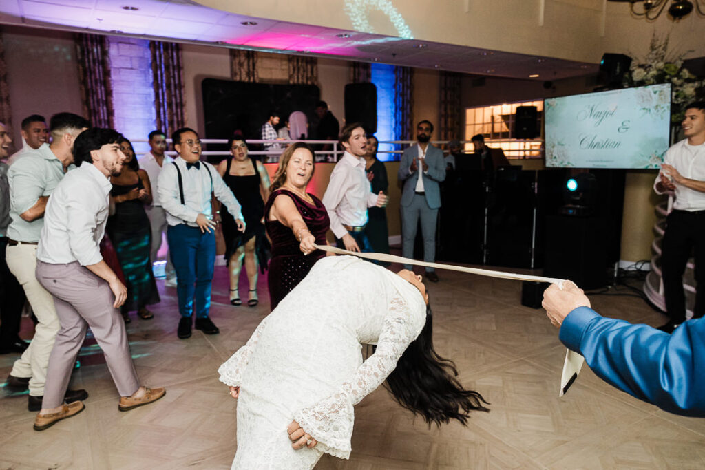 Guests cheering during a limbo dance on the wedding reception dance floor at The Armory NJ Restaurant in Perth Amboy, photographed by Alex Kaplan Photography.