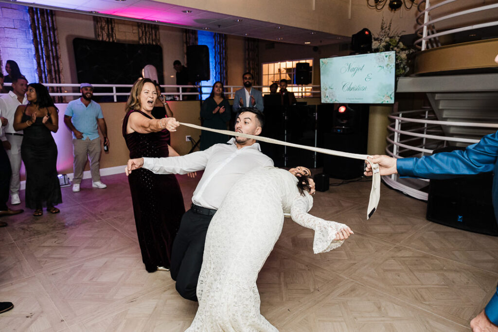 Guests laughing and playing limbo together on the dance floor during the wedding reception at The Armory NJ Restaurant in Perth Amboy, photographed by Alex Kaplan Photography.