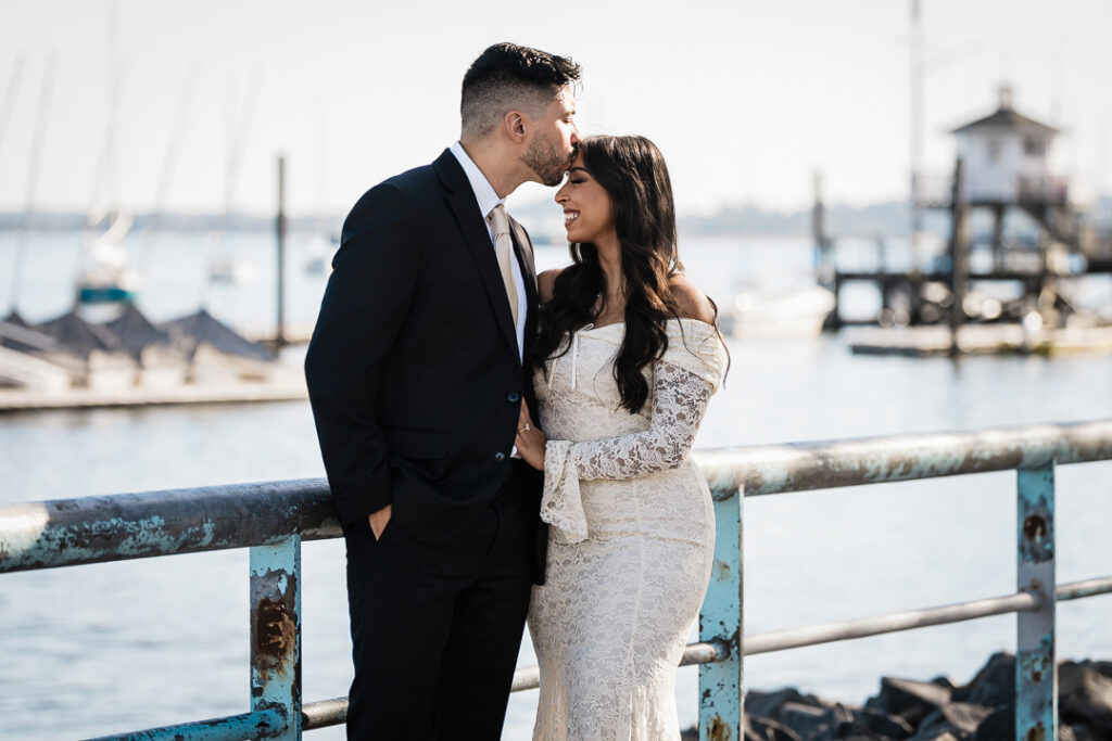 Engaged couple Navi and Christian sharing a romantic moment by the Perth Amboy waterfront, with sailboats and soft afternoon light behind them, captured by Alex Kaplan Photography at The Armory NJ Restaurant.