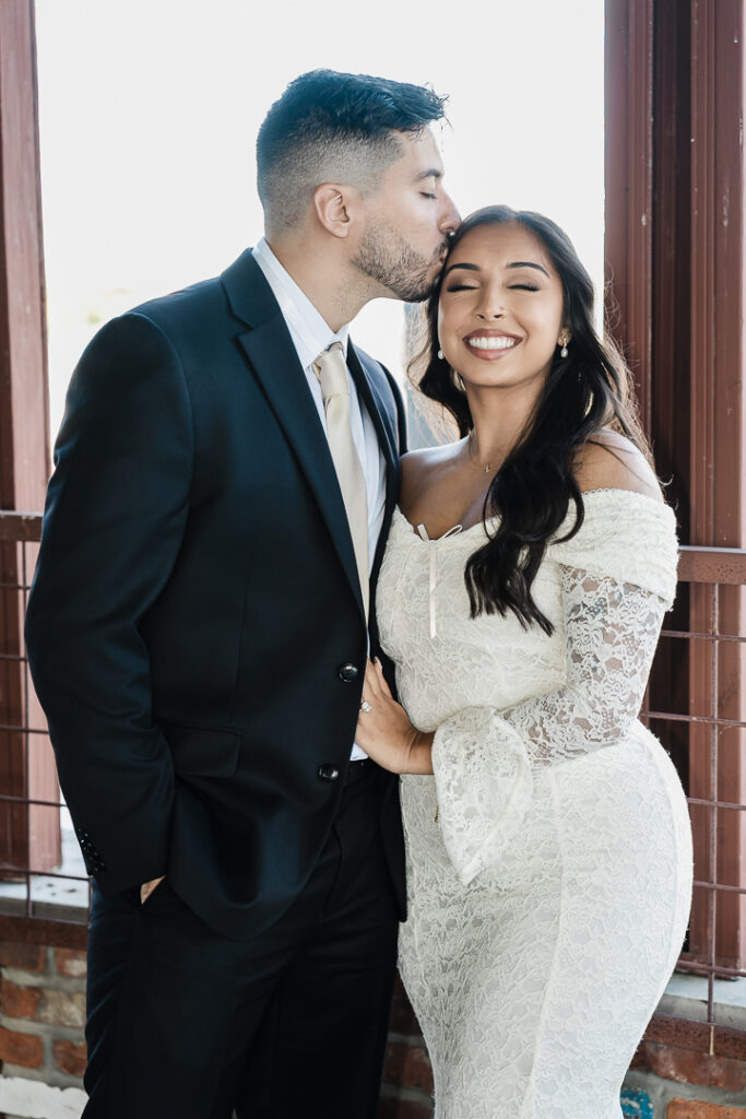 Groom-to-be kissing his fiancée on the forehead during a tender moment by the waterfront at The Armory NJ Restaurant in Perth Amboy, captured by Alex Kaplan Photography.