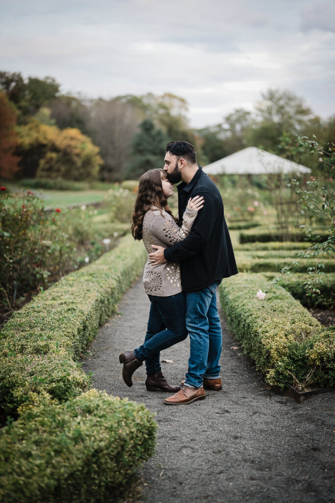 Romantic engagement kiss on garden pathway with formal gardens at Deep Cut Gardens Middletown NJ