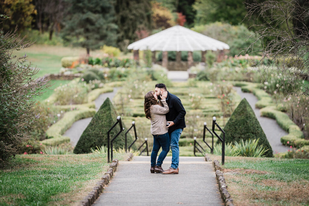 Couple kissing after surprise proposal at Deep Cut Gardens formal parterre gardens with gazebo - Middletown NJ proposal photographer