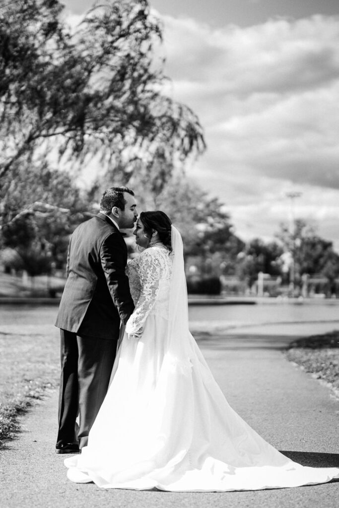 Intimate black and white portrait of couple kissing under willow tree.