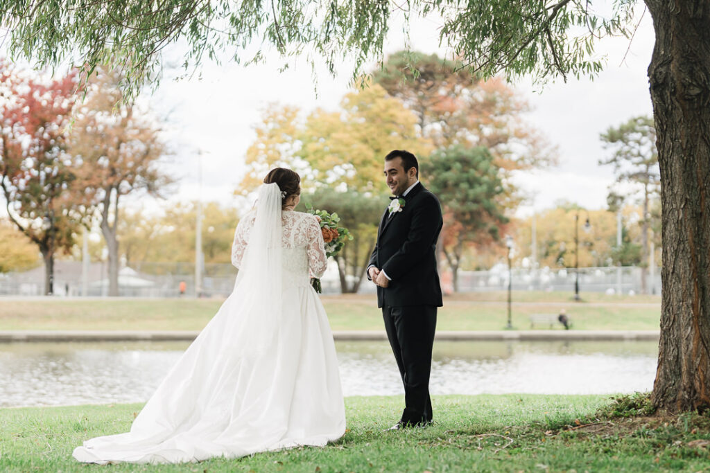 Bride approaching groom for first look under willow trees at Lincoln Park.