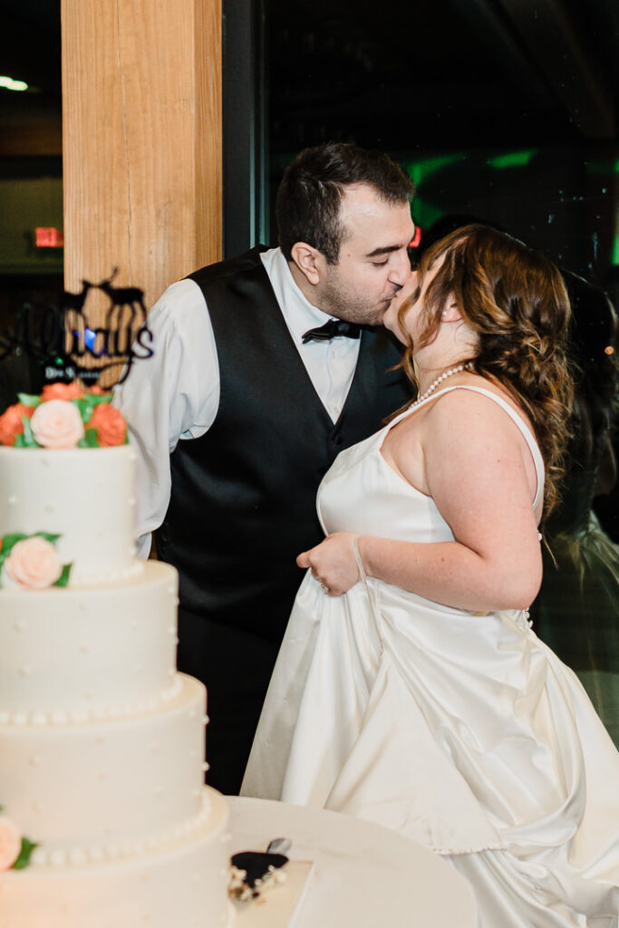 Bride and groom cutting white wedding cake with coral flowers.