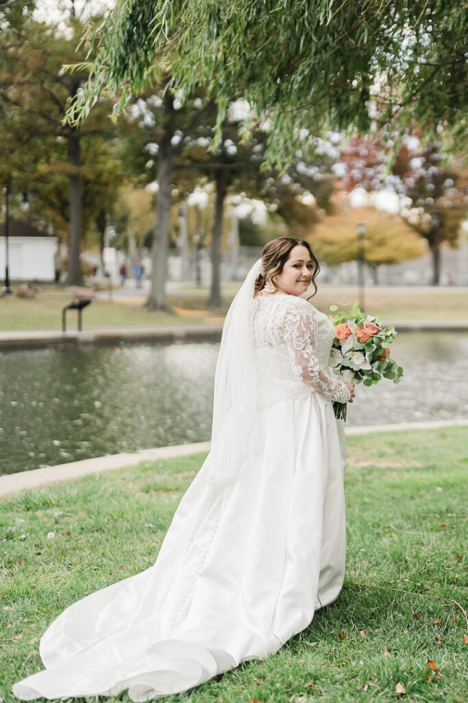 Bride in lace gown by Lincoln Park pond during fall wedding at The View, Jersey City.