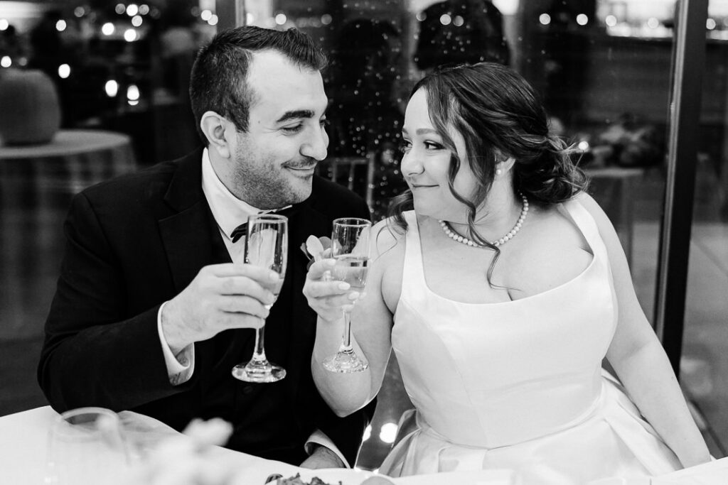 Intimate black and white moment of couple toasting champagne at sweetheart table.