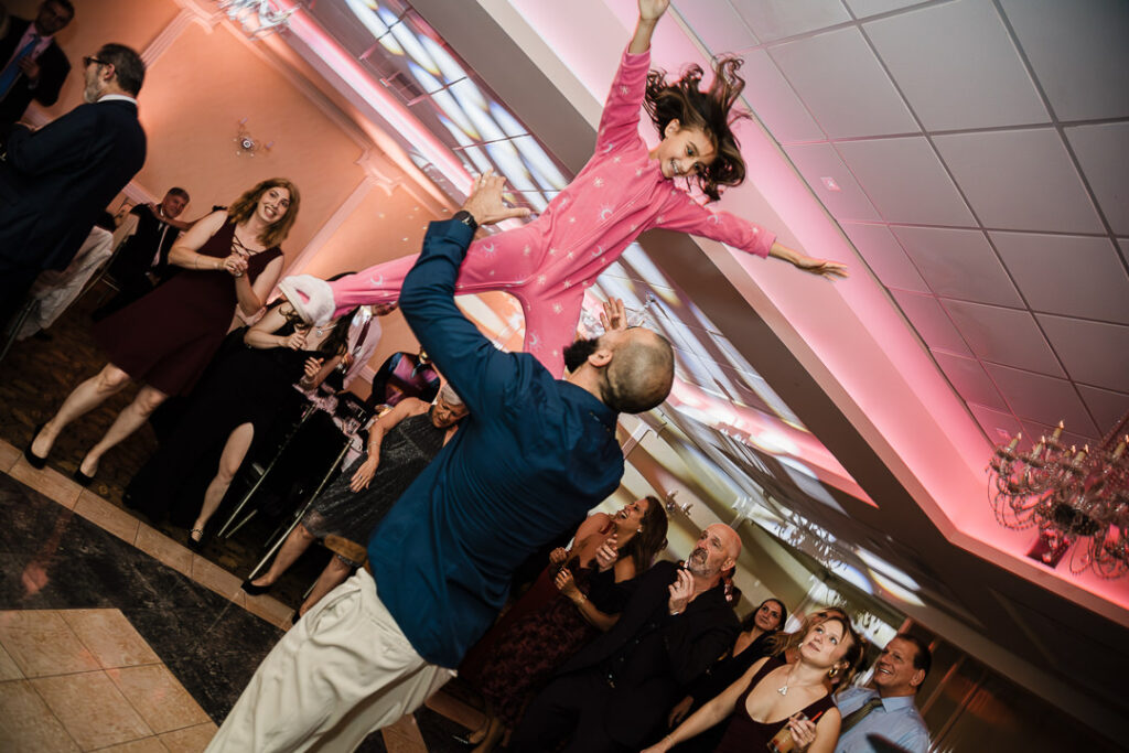 Wedding guest lifted in air on dance floor with pink uplighting Cortlandt Colonial Hudson Valley reception
