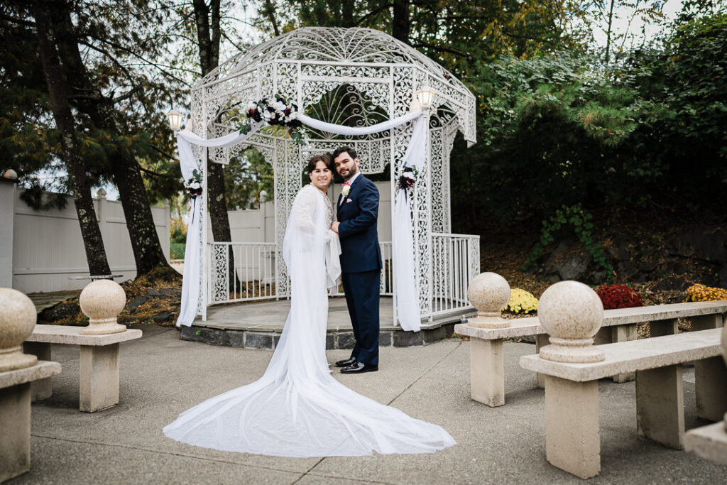 Couple standing at white Victorian gazebo with autumn florals during outdoor ceremony Cortlandt Colonial NY