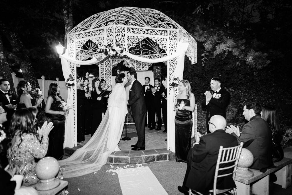 Black-and-white photo of first kiss under string lights Cortlandt Colonial fall wedding