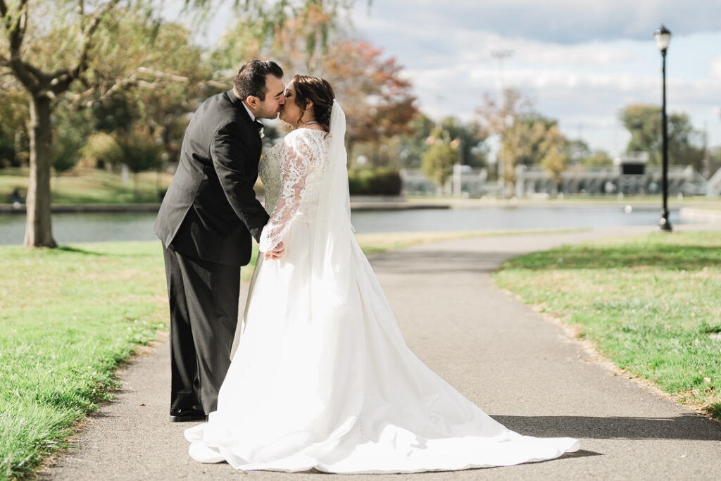 Bride and groom sharing a kiss on pathway with Lincoln Park pond behind them.
