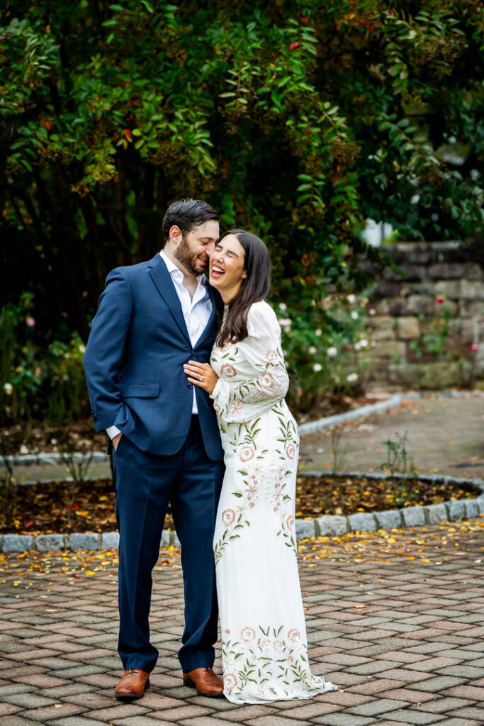 Engaged couple laughing in coordinated floral dress and navy suit on a garden path