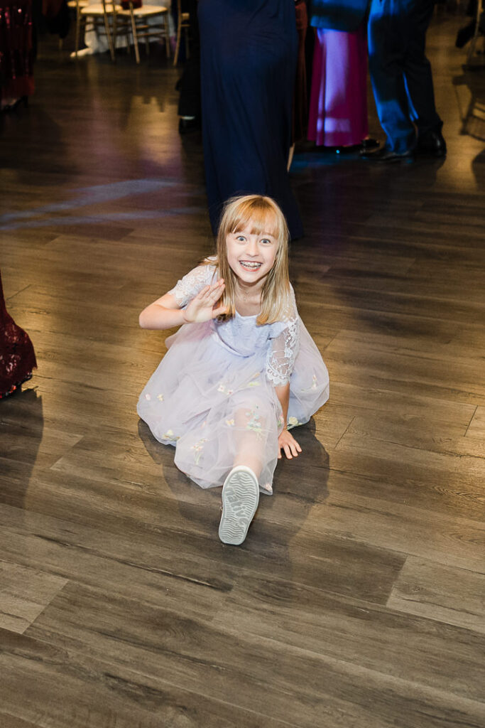 Young flower girl in lavender dress doing splits on dance floor.